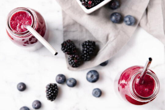 Berries fresh smoothies in glass bottles over a marble surface, overhead shot.