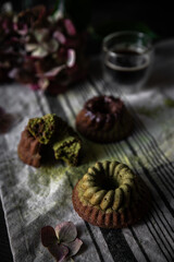 Fototapeta na wymiar Mini chocolate-matcha bundt cakes and hydrangea flowers on linen towel on dark background.