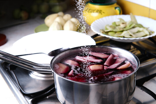 Unrecognizable cook adding sugar into saucepan with red wine and pears while preparing delicious  dessert at home