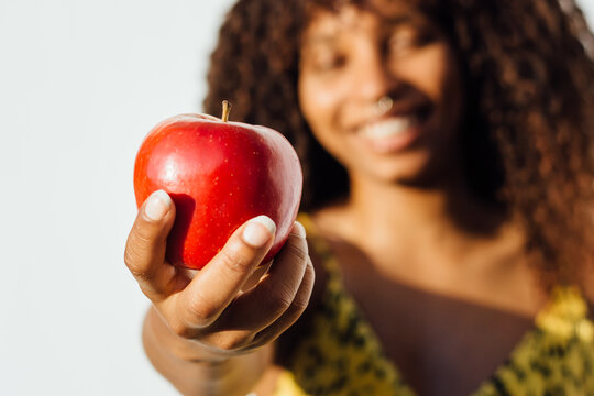 Blurred ethnic female standing with ripe red apple on white background in studio