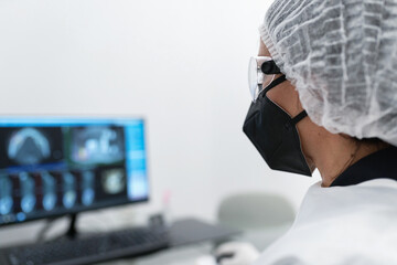 Side view of female medical specialist in protective mask and goggles working with scan image on computer monitor in modern clinic
