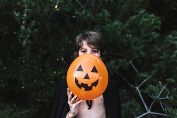 Portrait of boy holding pumpkin shaped balloon in front of his face while standing outdoors