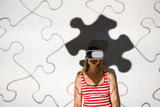 Unrecognizable young female in casual outfit and virtual reality goggles exploring cyberspace with puzzle pieces