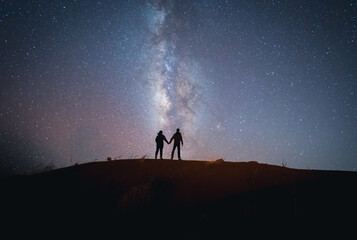 Scenic view of milky way in sky over couple standing on hill at night