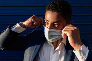Young African American male in formal outfit putting on medical mask for coronavirus prevention