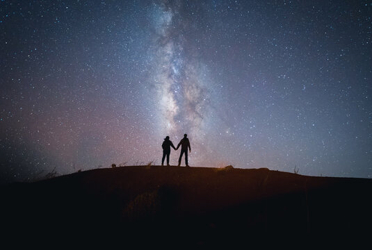 Scenic view of milky way in sky over couple standing on hill at night