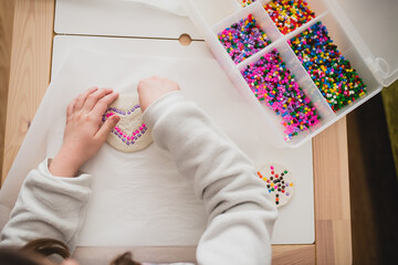 From above of unrecognizable child playing with colorful mosaic pieces while having fun at home