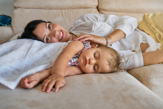 A little girl sleeping with her mother lying on a sofa while facing the camera