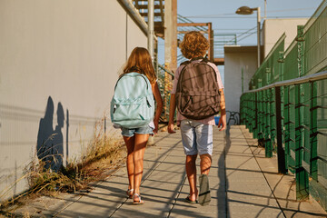 Two children with black school bags on their backs walking down an industrial passage going to school in the morning