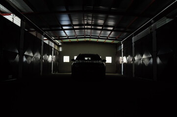 Fototapeta premium A parked car in a dark garage, where light comes from behind through small windows