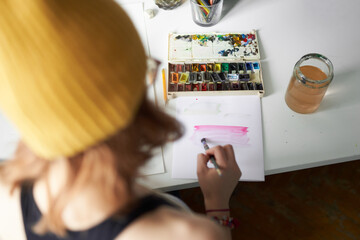 High angle back view of anonymous crop female painter creating aquarelle picture of color spectrum in workshop