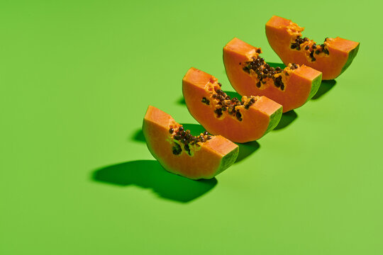 From above of cut pieces of fresh ripe sweet papaya fruit arranged in row on bright green background
