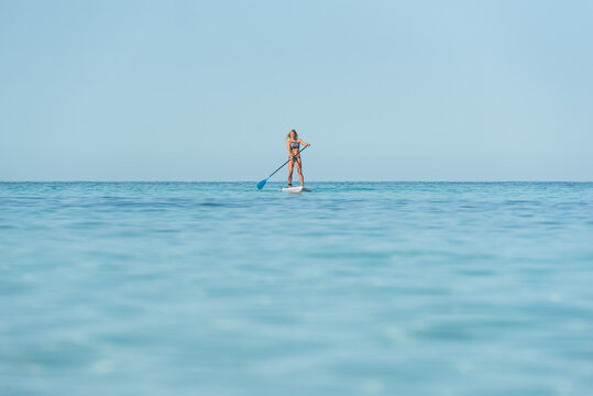 Ft female surfer in bikini standing on paddleboard and rowing while training in sea on sunny day