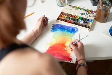 High angle back view of anonymous crop female painter creating aquarelle picture of color spectrum in workshop