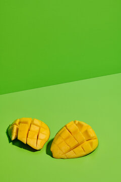 From above closeup of fresh ripe juicy mango half sliced into pieces on bright green background