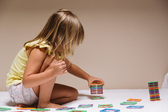 Side view of adorable preschool girl in eyeglasses sitting on floor and playing with colorful educational blocks