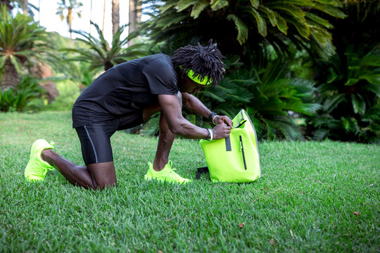 Side view of confident young African American male athlete with backpack in trendy sportswear getting ready to train in park with green tropical trees