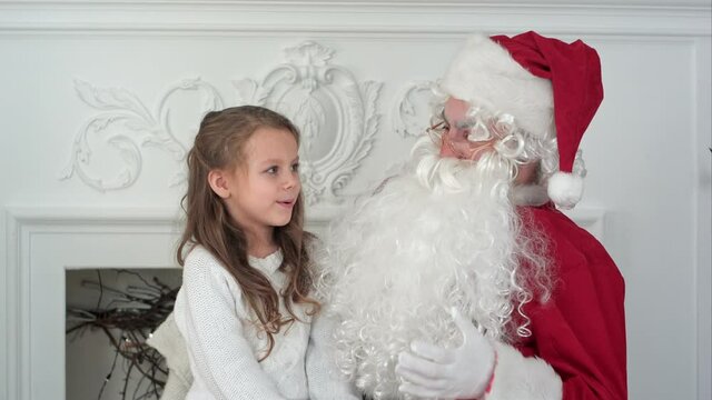 Cute little girl singing a Christmas song sitting on Santa Claus lap