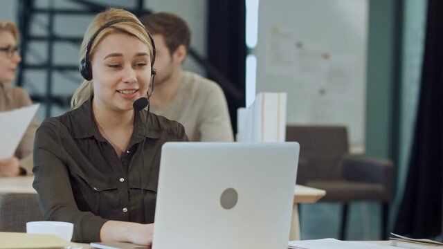 Smiling female helpline operator with headphones at her desk in the office