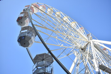 a white ferris wheel with colorful seats under blue sky in a sunny summer festival day 