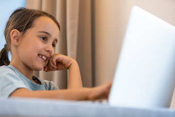 Little girl doing her homework at home and using a laptop