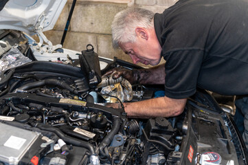 Senior Mechanic working on engine bay repairing a oil leak in home garage