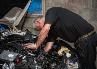 Senior Mechanic working on engine bay repairing a oil leak in home garage