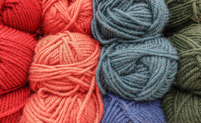 Colorful woolen balls of yarn. Background of colored yarn balls. Needlework. Knitting. Hobbies and leisure. Balls of yarn in red, orange, grey, blue and green colors.