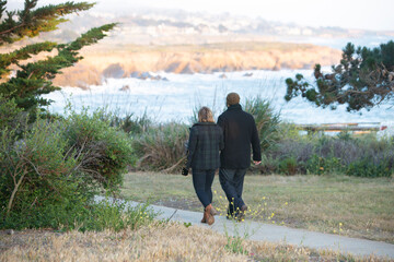 Male and female couple walking on path above the ocean wearing coats