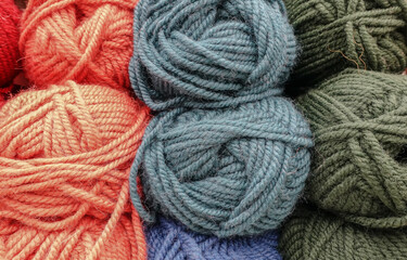 Colorful woolen balls of yarn. Background of colored yarn balls. Needlework. Knitting. Hobbies and leisure. Balls of yarn in orange, grey, green colors.