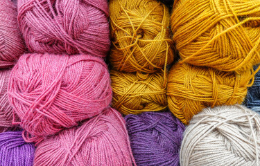 Colorful woolen balls of yarn. Background of colored yarn balls. Needlework. Knitting. Hobby and leisure. Balls of yarn in gold, white, pink colors.