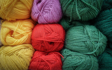 Colorful woolen balls of yarn. Background of colored yarn balls. Needlework. Knitting. Hobby and leisure. Balls of yarn in yellow, red, green and orchid colors.