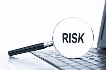 Magnifier with text RISK on laptop keyboard background