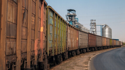 Fototapeta premium Many freight cars of the train stand next to large silos.