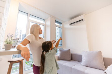 Happy family under air conditioner, mom holding remote control switch on conditioning in living...