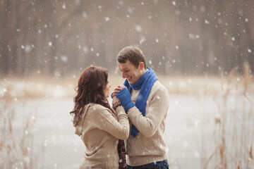 couple on winter walk in snow. Valentine's Day  for couple in rustic style. Happy couple in love warming themselves with tea under a blanket in the arms of nature. Casual outfit with Blue accessories