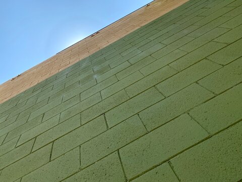 Detail of a green, cinder-block wall with blue sky in background, creating abstract, background texture