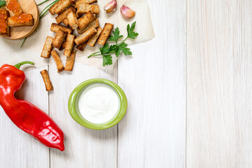 Slices of fried croutons with sour cream sauce, red pepper, caviar and garlic cloves close up on a white wooden boards. Flat lay. Copy space.