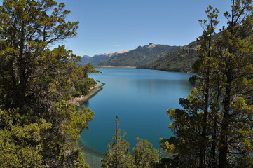 Fototapeta na wymiar Amazing view of a lake with calm waters, surrounded by forest-covered mountains in Patagonia. Behind are snow-capped mountains