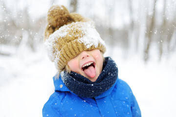 Funny little boy in blue winter clothes walks during a snowfall. Outdoors winter activities for kids.