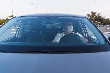 Obraz premium Chico con mascarilla dentro de coche en asiento de conductor