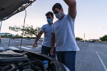 Dos hombres con mascarilla revisando motor de un coche