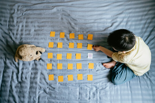 Asian kid playing matching game with his stuffed animal on his bed