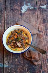 Single bowl of polenta with mushrooms on a wooden background