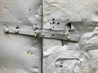 the door is metal, painted in gray paint. a builder's booth with a makeshift castle. texture with metal inserts, hooks. metal sheet with holes, damage, rust and corrosion