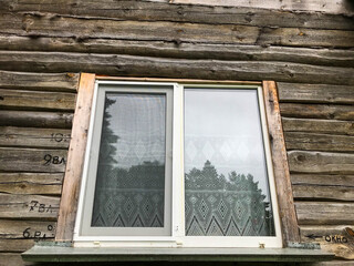 the window is wooden in the frame. wooden house in the village. glass window with painted wooden frame. there is a curtain hanging on the window, tulle made of white thin material