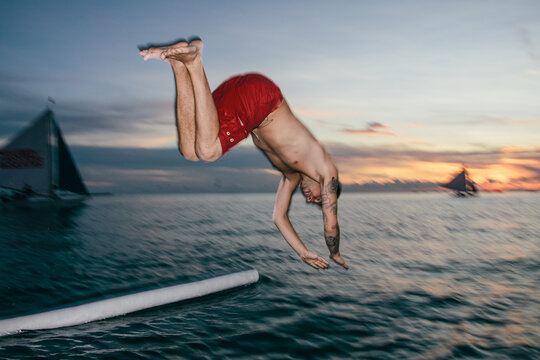 Young man diving into the water of the sea from a boat at sunset