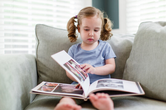 Toddler looking through a photo album while sitting in a big chair