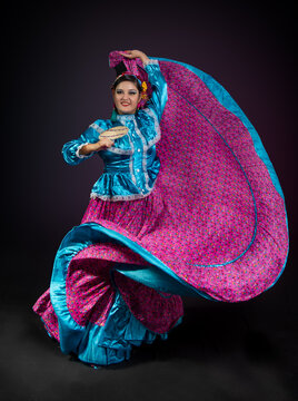 Mujer bailarina de folklor mexicano del estado de nayarit, traje folklorico nayarrita color rosa mexicano con azul, abanico y bailando con faldeo y vueltas sobre fondo negro