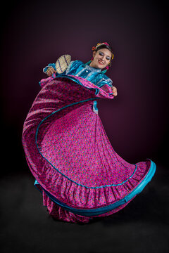 Mujer bailarina de folklor mexicano del estado de nayarit, traje folklorico nayarrita color rosa mexicano con azul, abanico y bailando con faldeo y vueltas sobre fondo negro